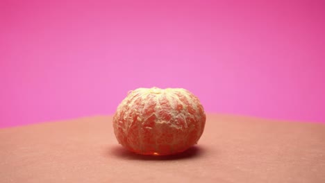 Mandarina-Madura-Pelada,-Gire-En-Video-De-4k-De-Fondo-De-Papel-Rosa-Y-Viejo-Con-Corrección-De-Color