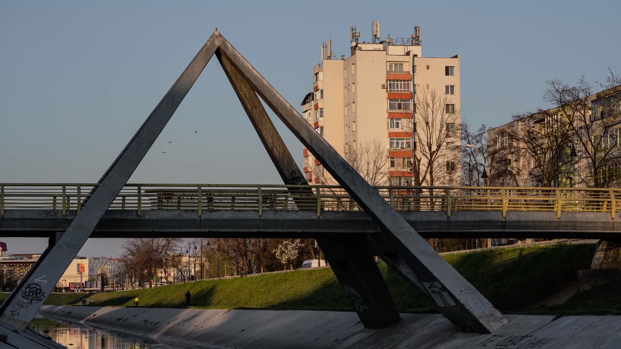 lapso de tiempo al atardecer que muestra un paisaje urbano, gente cruzando un puente triangular y movimiento de pájaros