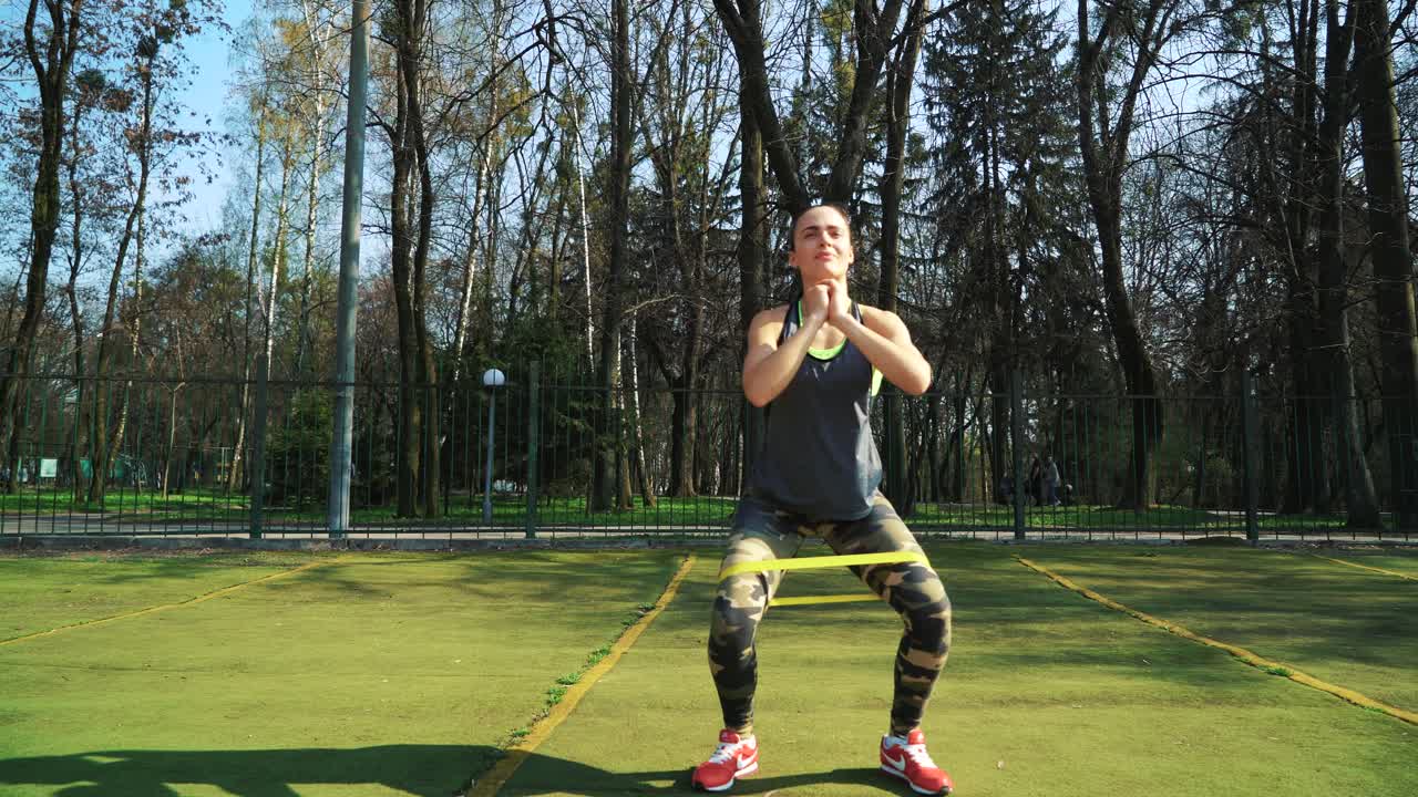 Woman doing exercises outdoors at the stadium. Beautiful young woman working with elastic band. Fitness concept.