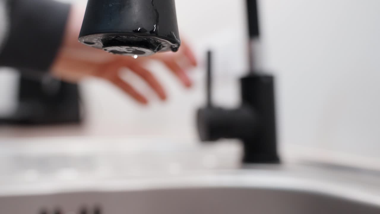 Persona che chiude un rubinetto di lusso nero, gocce d'acqua