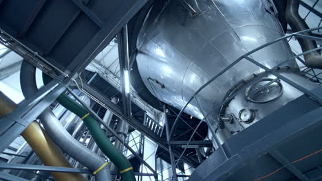 huge dairy tank beside the thick plastic tubes. stainless steel tank standing at the raised platform with sensors at its basics. circle view from below.