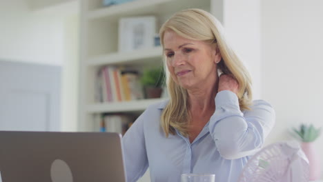 menopausal mature woman suffering neck pain working on laptop at home