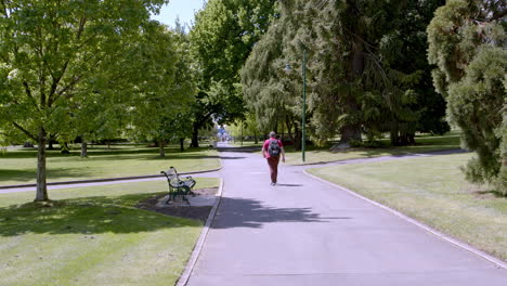 hombre no identificado caminando por la carretera en medio del parque de la ciudad con árboles sombreados