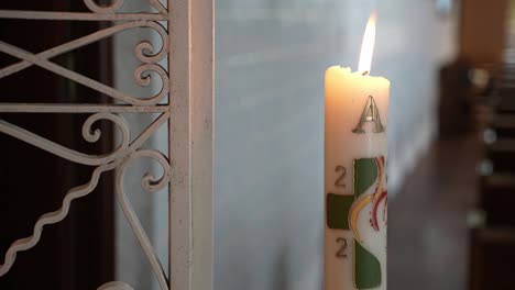 Paschal-candle-with-symbols-and-burning-flame-inside-church---closeup