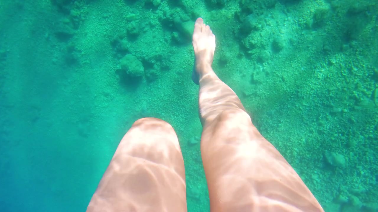 First person POV of legs above crystal clear turquoise seawater during a summer vacation.