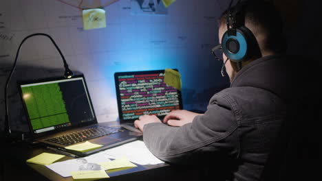 joven caucásico con auriculares iluminados escribiendo en el teclado de un portátil