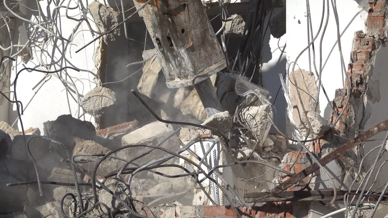 An excavator demolishing concrete building with hydraulic breaker in daylight