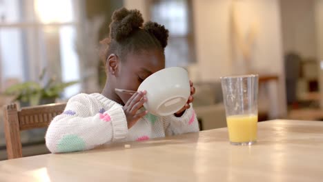 African-american-girl-eating-cereal-with-milk-in-kitchen,-slow-motion