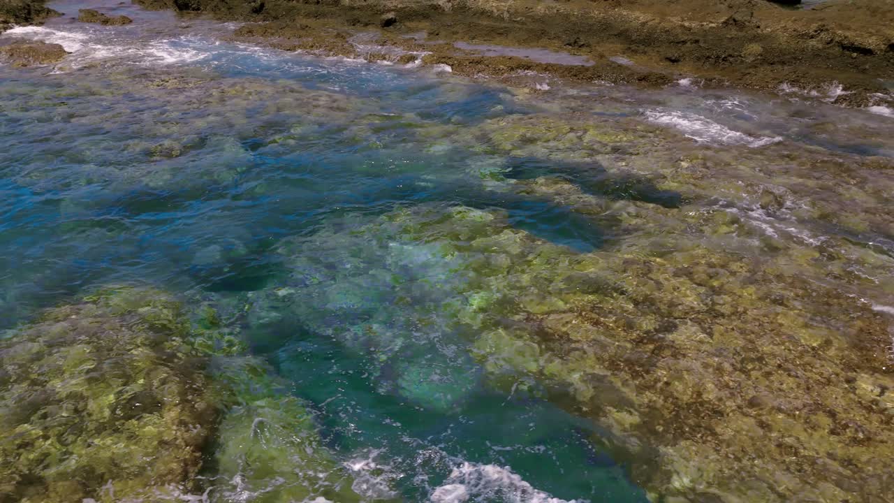 Waves crash on volcanic rocks in Tenerife's Alcalá under clear sky