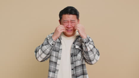 upset disappointed asian man wipes tears and cries from despair being sad because of unfair things