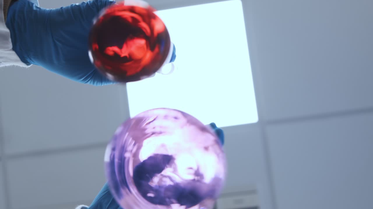 científico con guantes de goma y bata de laboratorio mezclando líquidos rosados en los frascos de vidrio