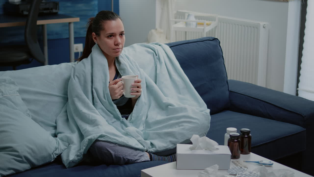 Sick woman holding cup of tea and sitting in blanket