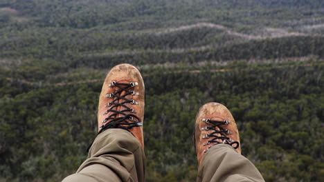 Old-worn-leather-hiker's-boots-hanging-over-edge-of-cliff-and-moving-slowly-with-wilderness-stretching-out-into-distance