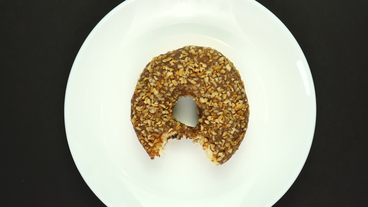 rosquilla mordida cubierta de glaseado de chocolate con salpicaduras en un plato blanco giratorio