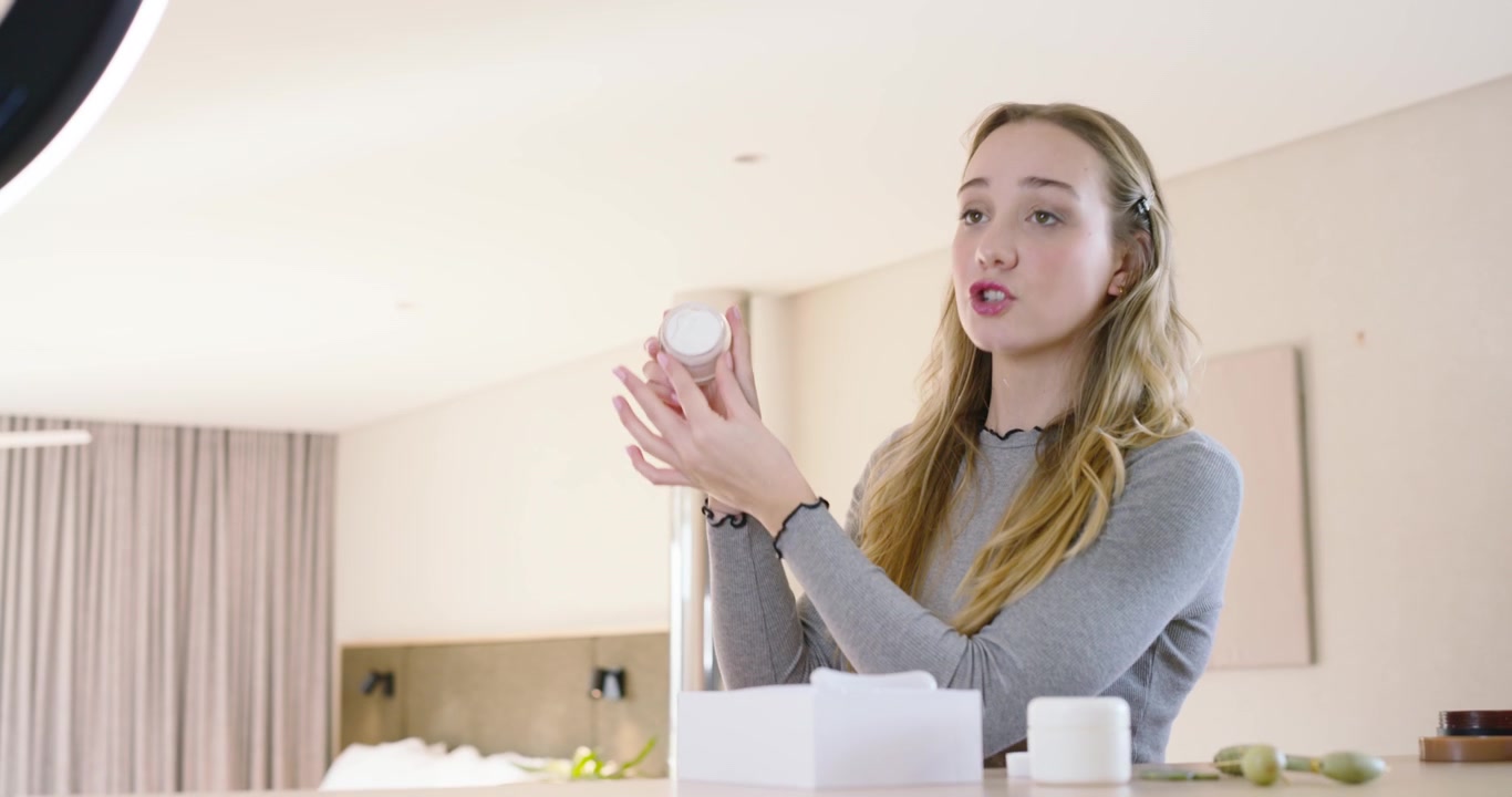 Donna che mostra, strofina la crema, apre il barattolo, applica sotto gli occhi alla toeletta dell'hotel con una ring light.