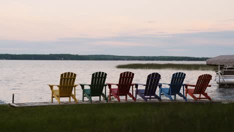 six-colorful-Adirondack-chairs-neatly-set-up-looking-out-at-a-lake-during-sunset