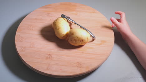 Hands-of-little-girl-peeling-potatoes-with-peeler-on-wooden-desk,-childhood-and-domestic-help-concept