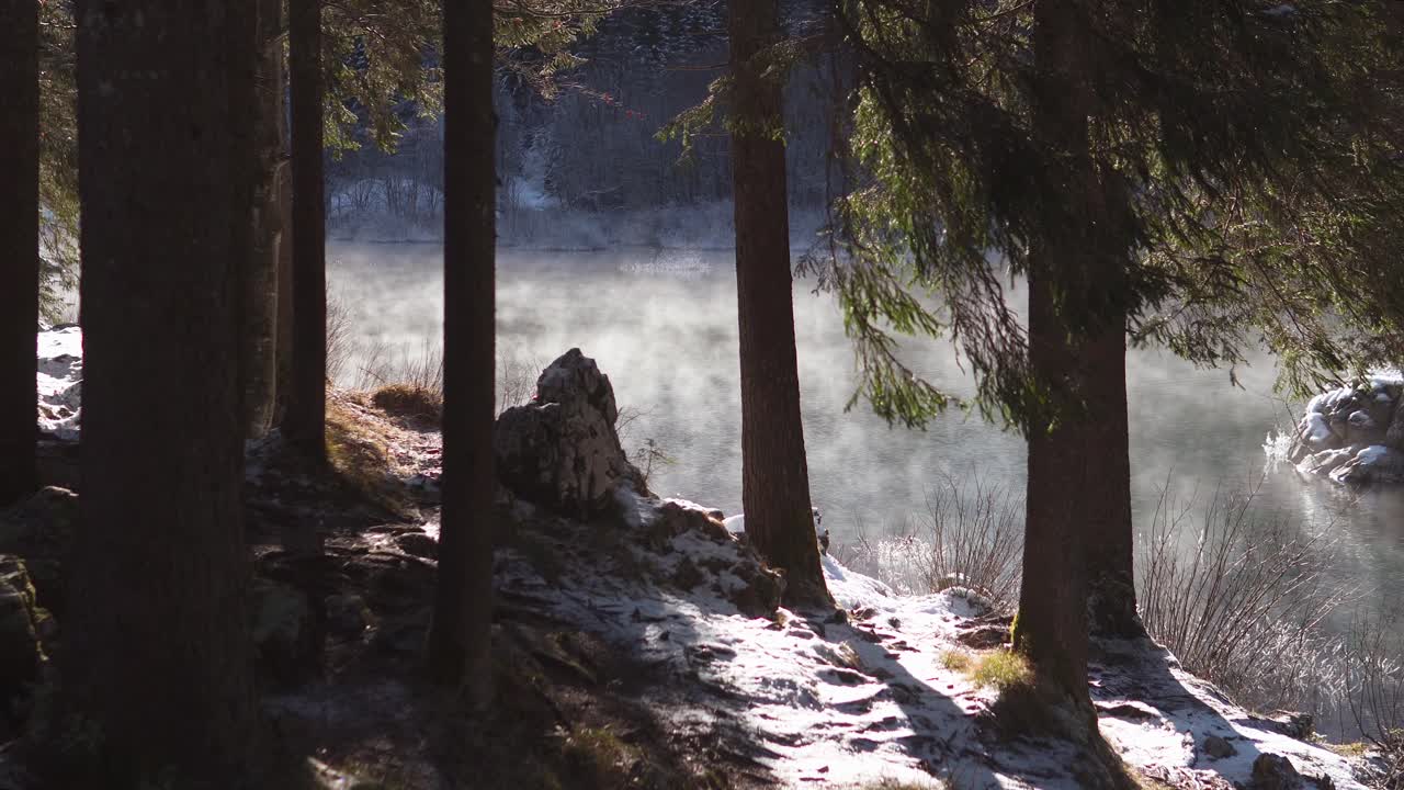View on mist rising from Alpine lake from snowy foresty lakeshore on sunny morning