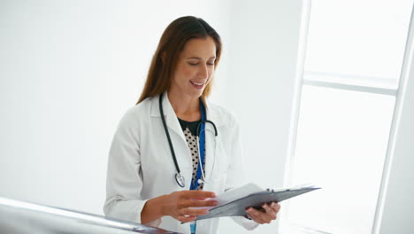 Female-Doctor-With-Clipboard-Checking-Patient-Notes-On-Stairs-In-Hospital