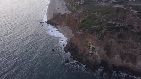 AERIAL:-flight-over-Malibu,-California-view-of-beach-Shore-Line-Pacific-ocean-at-sunset-with-mountain-cliff