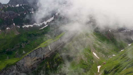 Tiro-De-Dron-En-ángulo-Descendente-De-Altenalp-Turm,-Con-Nubes-Que-Cubren-La-Ladera-De-La-Montaña