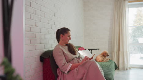 woman sitting on couch with dog beside her, operating her phone in cozy room with television table and cotton curtains, creating a peaceful moment of relaxation and connection with pet