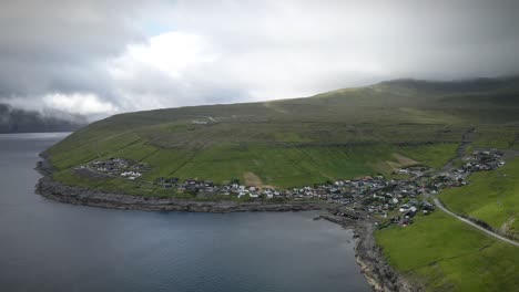 kvívík, un pintoresco pueblo en la escarpada costa de la isla de streymoy, con casas de colores, campos verdes y montañas dramáticas bajo un cielo nublado, drone estableciendo la toma