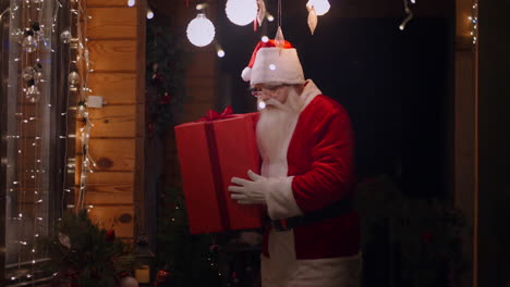 Santa-Claus-with-a-gift-in-his-hands-comes-to-the-window-and-looks-through-the-garland-into-the-house-to-bring-the-gift-and-put-it-under-the-tree.