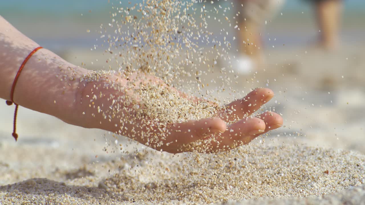 Sand som faller från en hand i slow motion på en strand. Koncept för semester och resor. Filmat med super slow motion-kamera 1000 fps