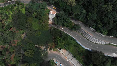 Hairpin-bends-in-Yercaud,-India-covered-with-endless-vast-green-forest-with-trees-growing-rapidly-vehicles-passing-on-the-road-top-view
