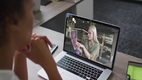 mid section of african american woman having a video call on laptop with female colleague at office