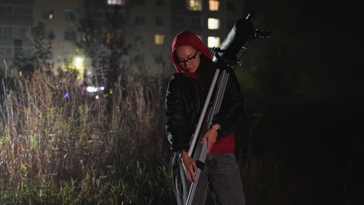 night field stargazer with telescope adjusting tripod near apartment lights, hooded observer prepares scope, silent urban outskirts, grass and weeds backlit by city glow, patient scientific curiosity