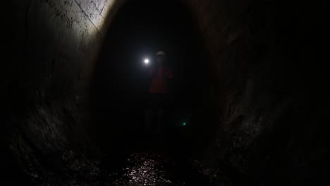 person exploring a dark tunnel with a flashlight