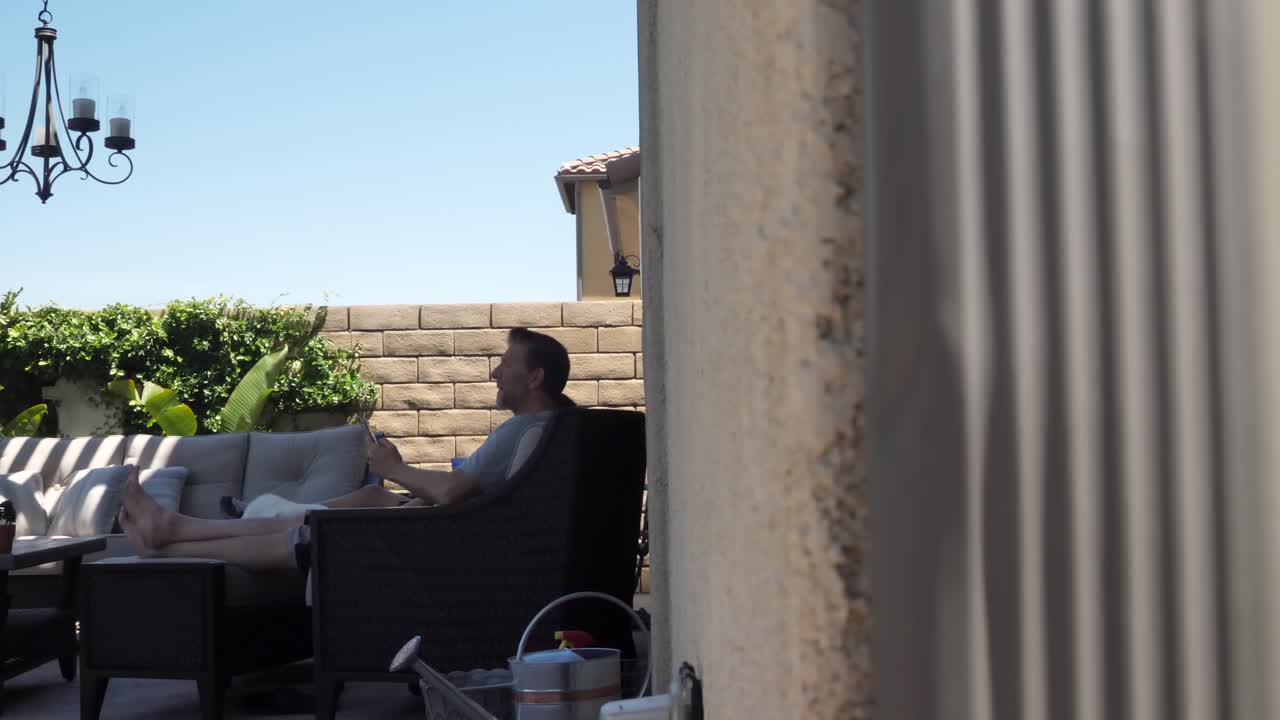 Male on phone sat outside in backyard on sunny day with pet dog, slider reveal