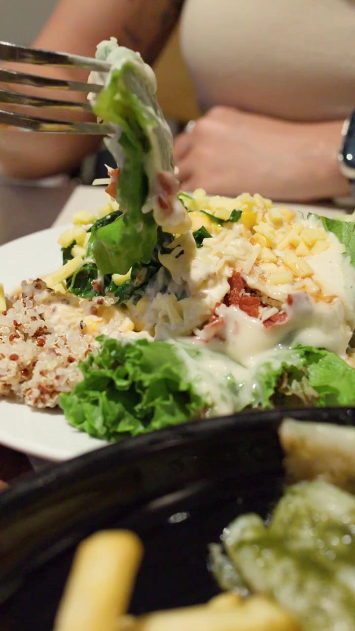 Close-up de mulher comendo salada fresca de quinoa com folhas verdes, vegetais, molho cremoso, câmera na mão