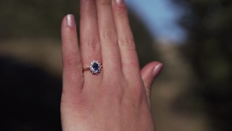 New-engaged-woman-showing-off-wedding-ring-with-diamonds-and-sapphire-stone-shimmering-and-reflecting-in-the-sunlight-in-forest