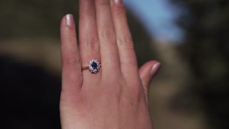 new engaged woman showing off wedding ring with diamonds and sapphire stone shimmering and reflecting in the sunlight in forest