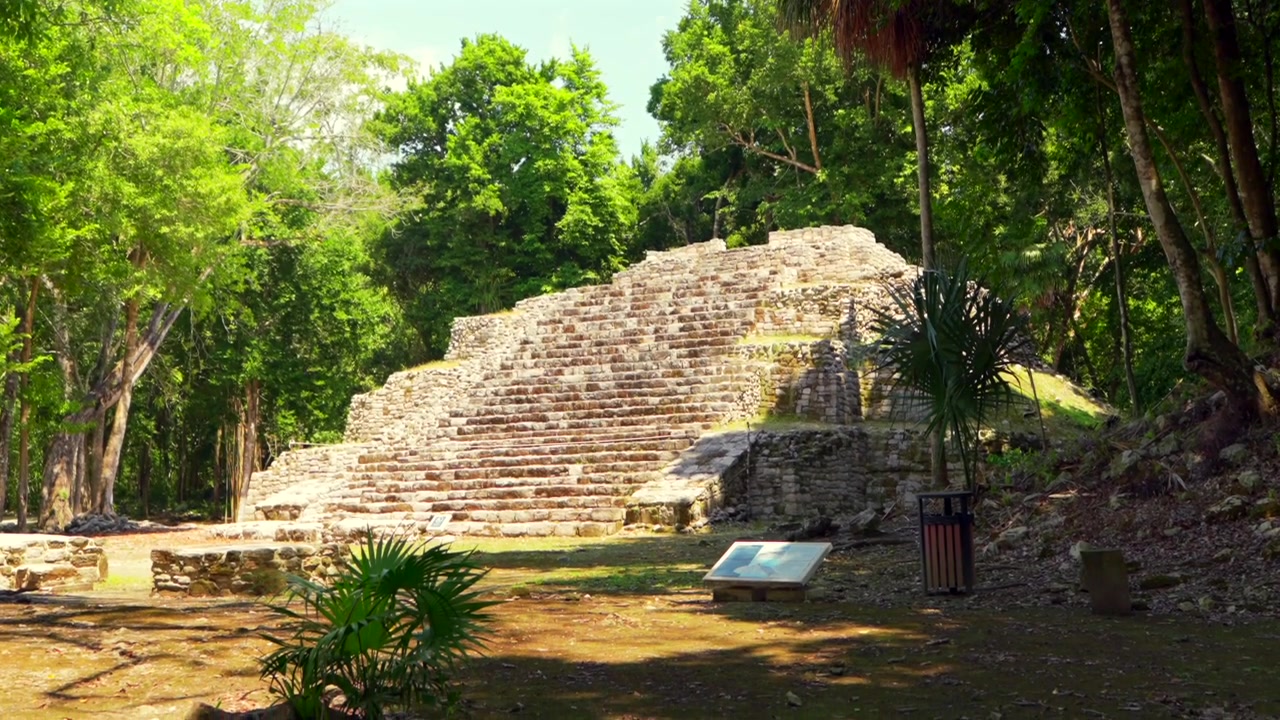 Un'affascinante ripresa in picchiata rivela l'antico tempio Maya nella Zona Archeologica di Oxtankah, circondato da una vivace vegetazione della giungla sotto un cielo sereno. Rovine storiche