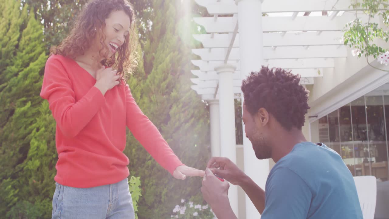 Happy biracial man proposing on knees with ring to surprised woman