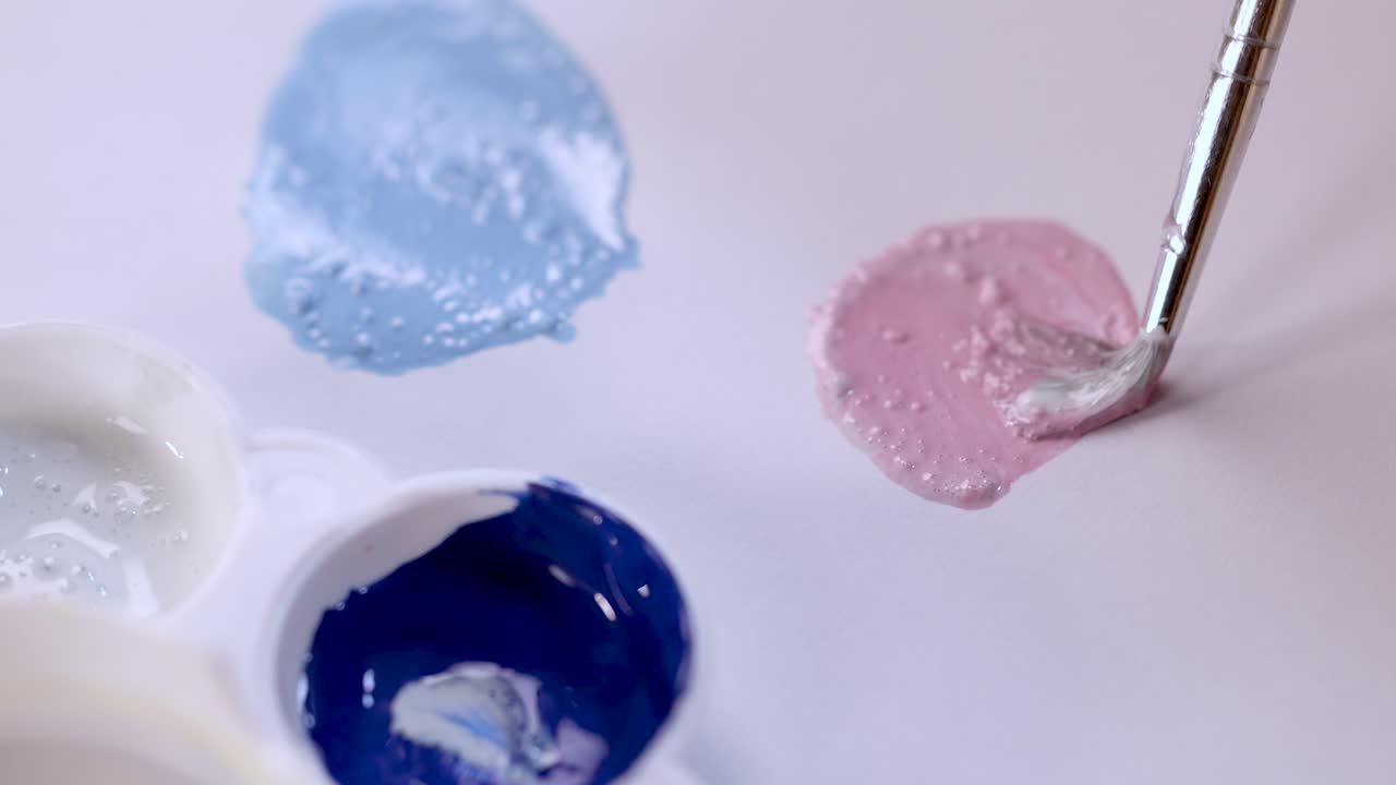 Artist uses brush to blend pink paint on palette under soft, diffused natural lighting