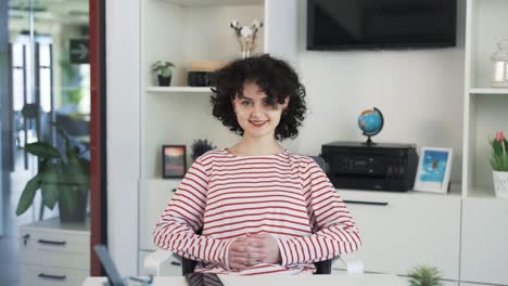 Portrait-of-a-beautiful-young-curly-haired-girl-sitting-at-a-desk-with-a-laptop-in-a-nice-bright-office-and-smiling-into-the-camera