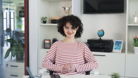 portrait of a beautiful young curly-haired girl sitting at a desk with a laptop in a nice bright office and smiling into the camera