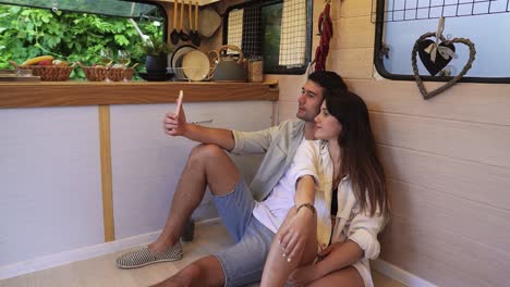 beautiful couple sitting on the floor in the stylish kitchen in van and doing selfie using smartphone, posing . enjoying togetherness, shared holidays, traveling by wheels house. modern interior