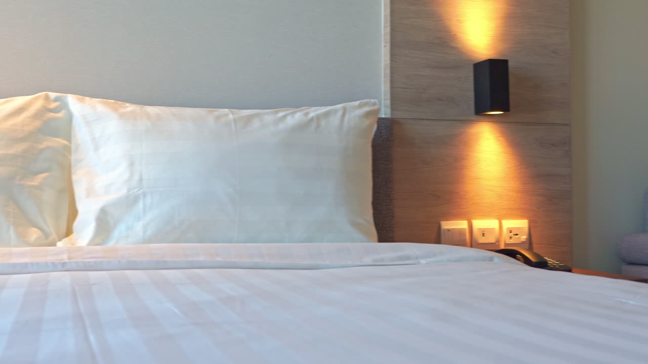 Kamar tidur hotel dengan sofa bed abu-abu kosong dengan dua bantal sofa dan tempat tidur putih bersih dengan bantal