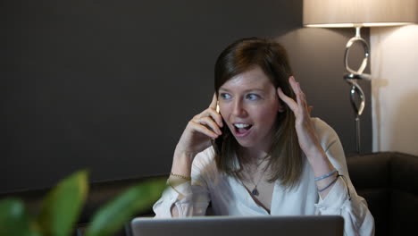 excited young professional woman receiving good new working at home talking on the phone in front of a laptop