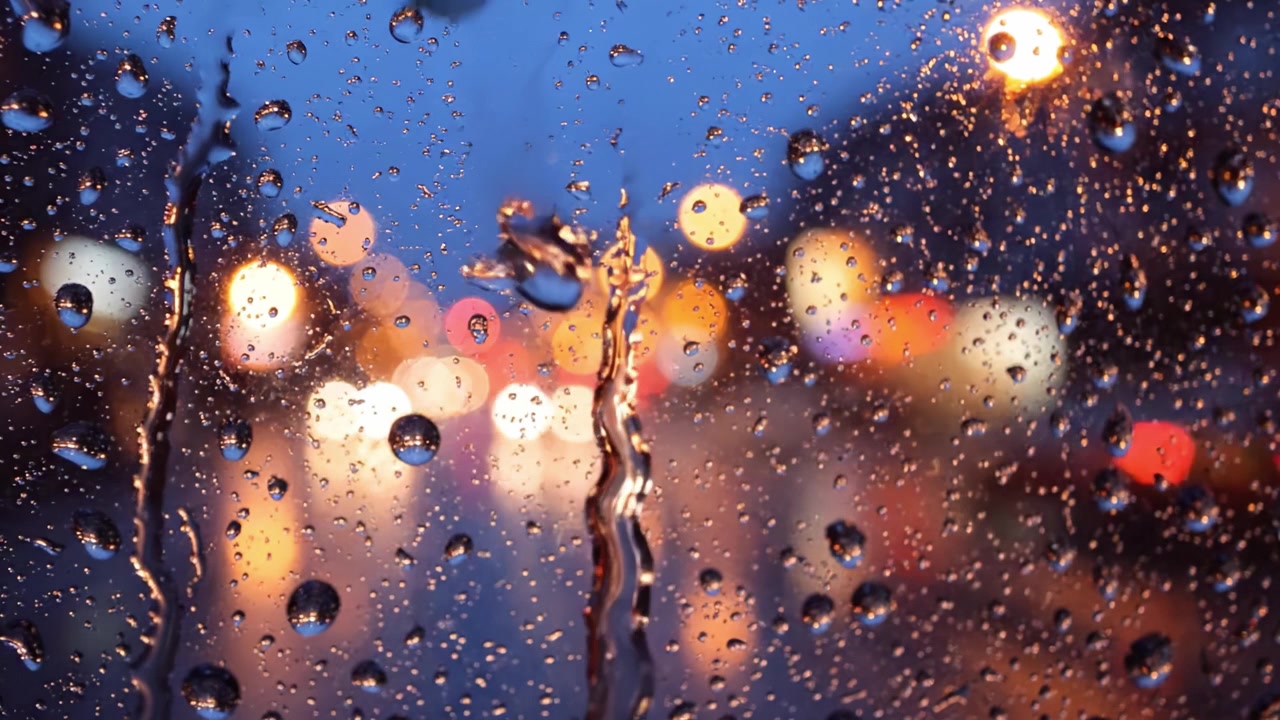 Ein fesselnder Blick auf Regentropfen an einem Fenster vor einer nächtlichen Stadtlandschaft: Schimmernde Lichter und reflektierende Oberflächen schaffen eine verträumte Atmosphäre