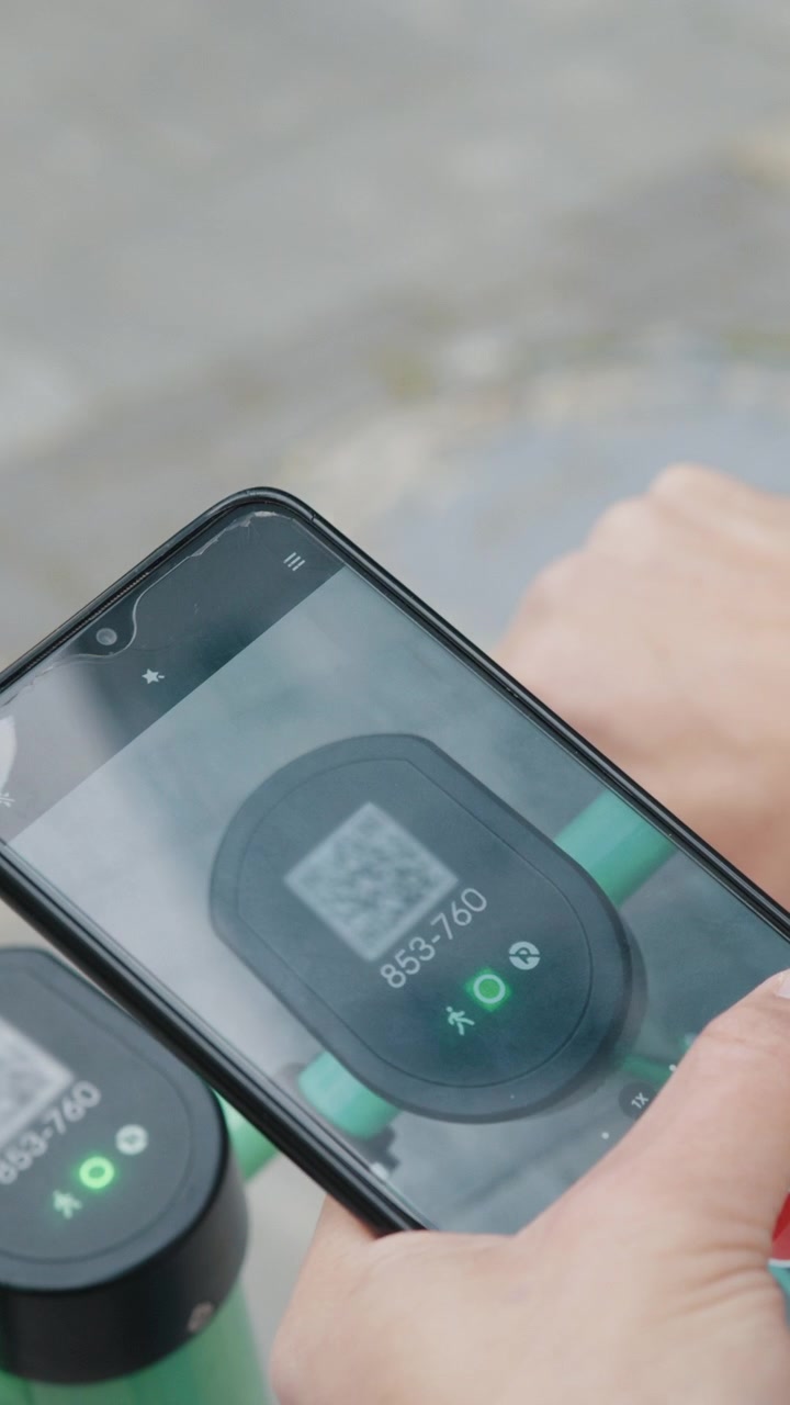 Una persona sta usando uno smartphone per scansionare un codice QR su uno scooter elettrico, probabilmente per sbloccarlo o attivarlo.