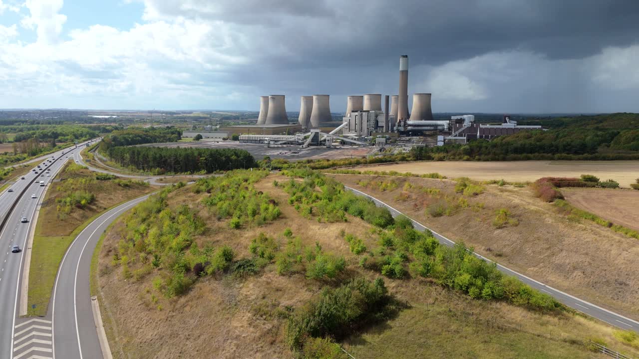 Aerial drone view of huge coal-fired power plant with cooling towers, chimney stacks, pylons and busy motorway revealing industrial landscape near Nottingham, United Kingdom