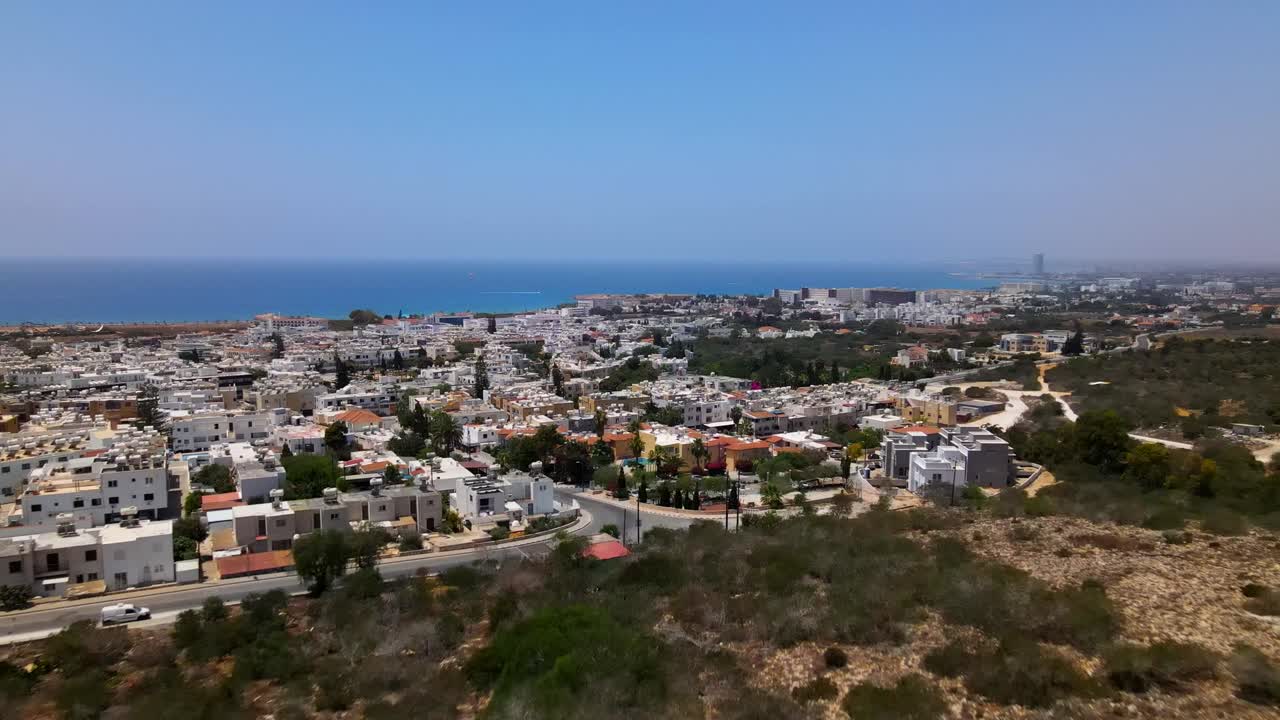Drone footage captures scenic Sarandë cityscape with rugged rocky foreground and vast Mediterranean horizon. Bright daylight enhances vibrant urban and natural contrast
