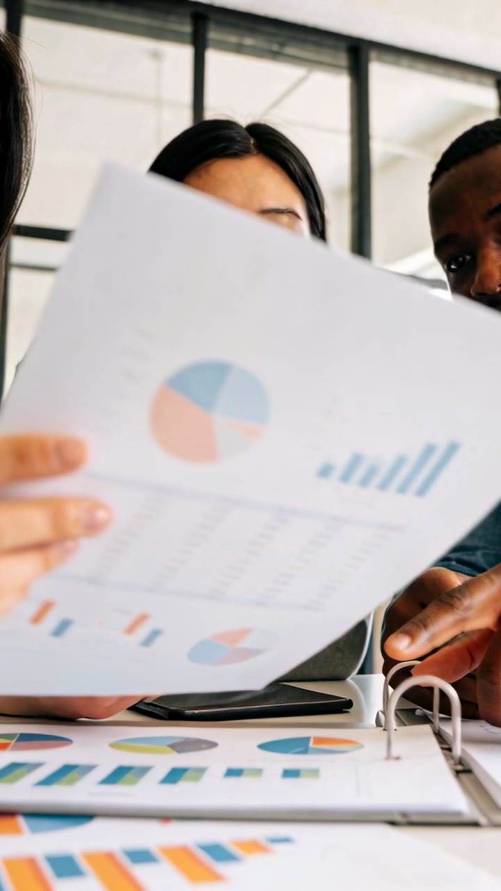 Vertical video: Team flipping charts at meeting, exposing binder and phone, reviewing business data